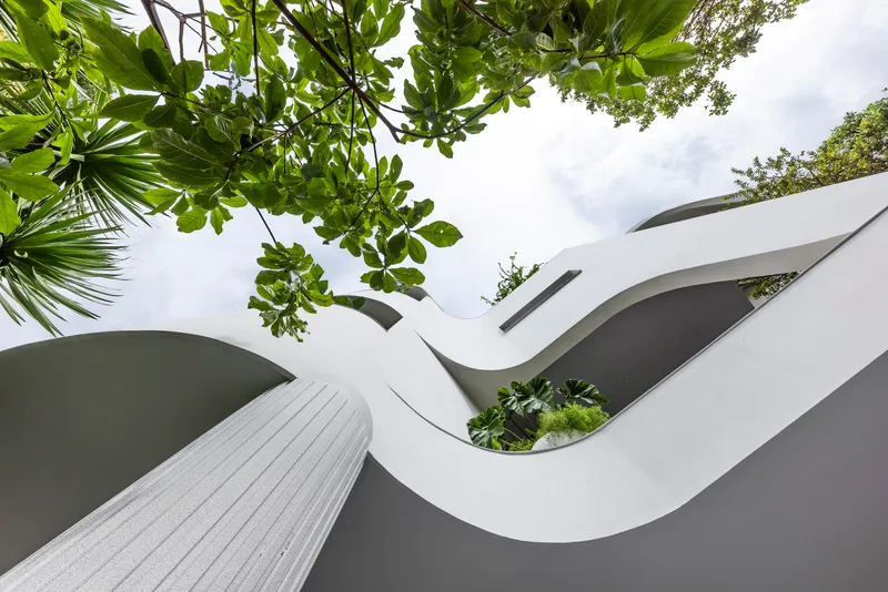 Worm's eye view of undulating white roof forms with planted openings framed by tropical foliage