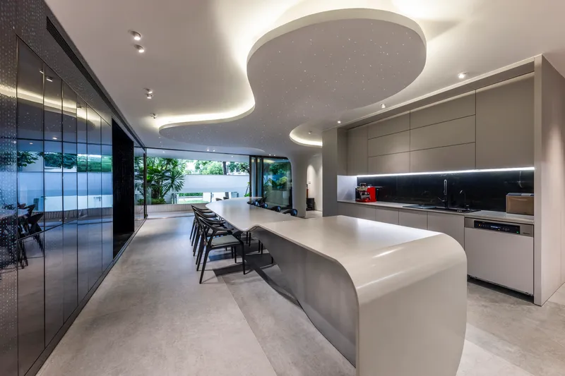 Kitchen and dining space with curved island beneath an organic ceiling cutout overlooking the courtyard