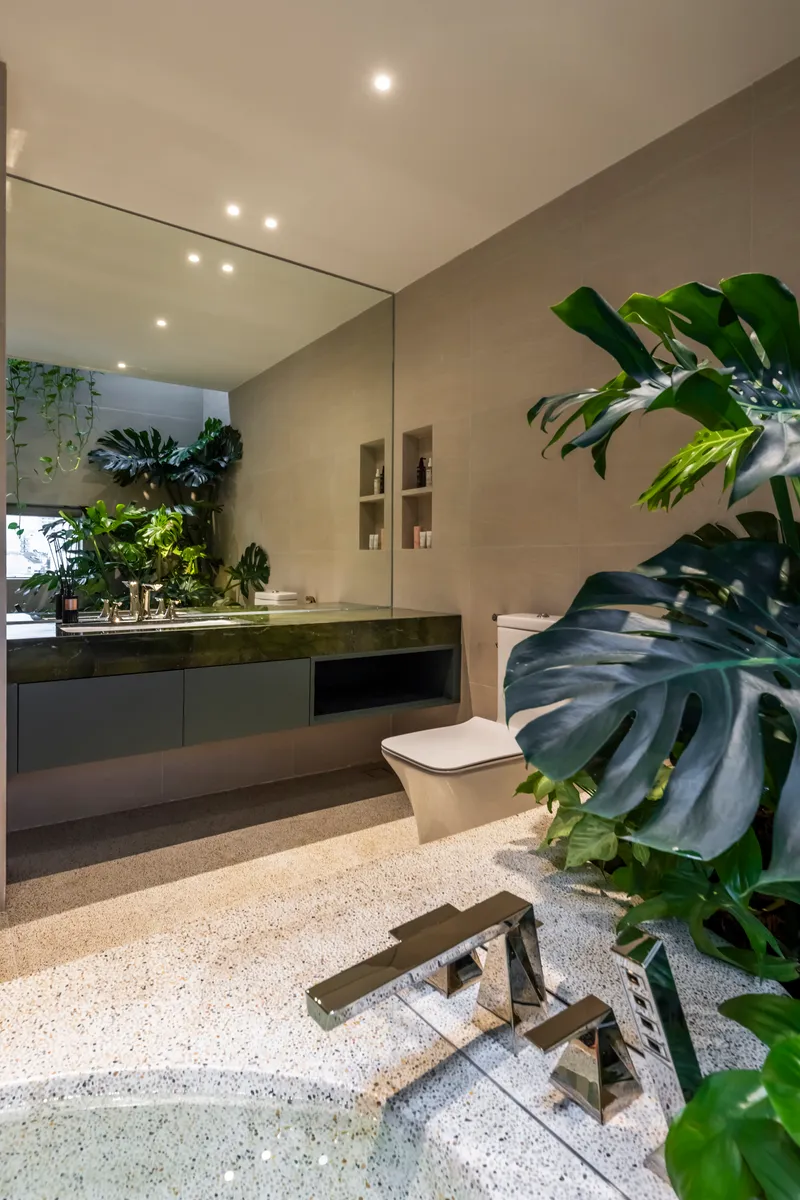 Bathroom vanity with floating mirror and tropical foliage beside terrazzo flooring and timber stepping stones