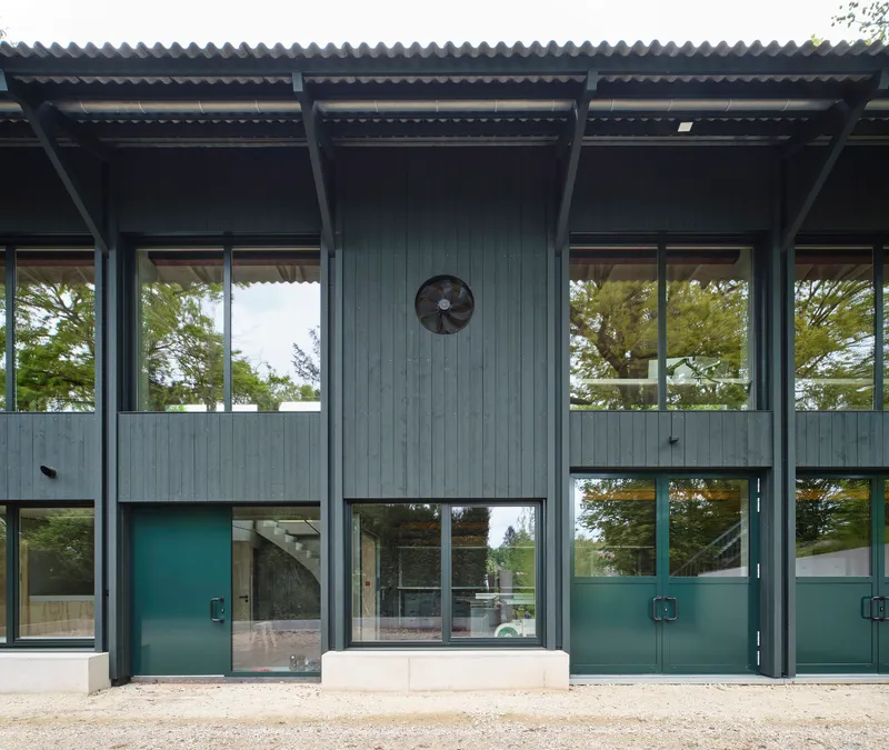 Facade with corrugated metal roof overhang and large glazed panels separated by teal-painted steel doors