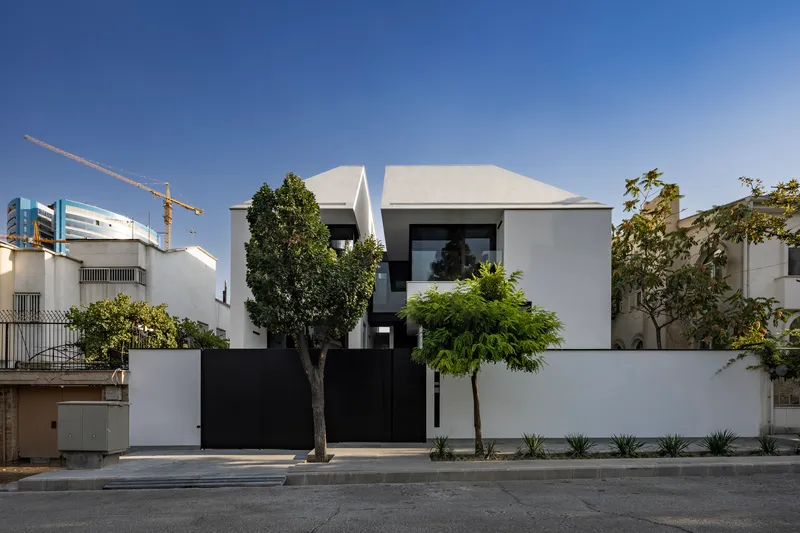 Street view of the white stucco facade with black metal gate and planted trees along the sidewalk