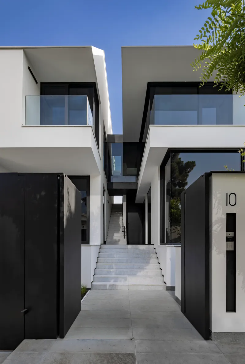 Entry passage with stone pavers between two angled white volumes and black metal doors