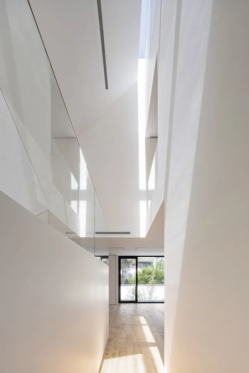 Triple-height skylight shaft with white walls and wood flooring below in bright daylight