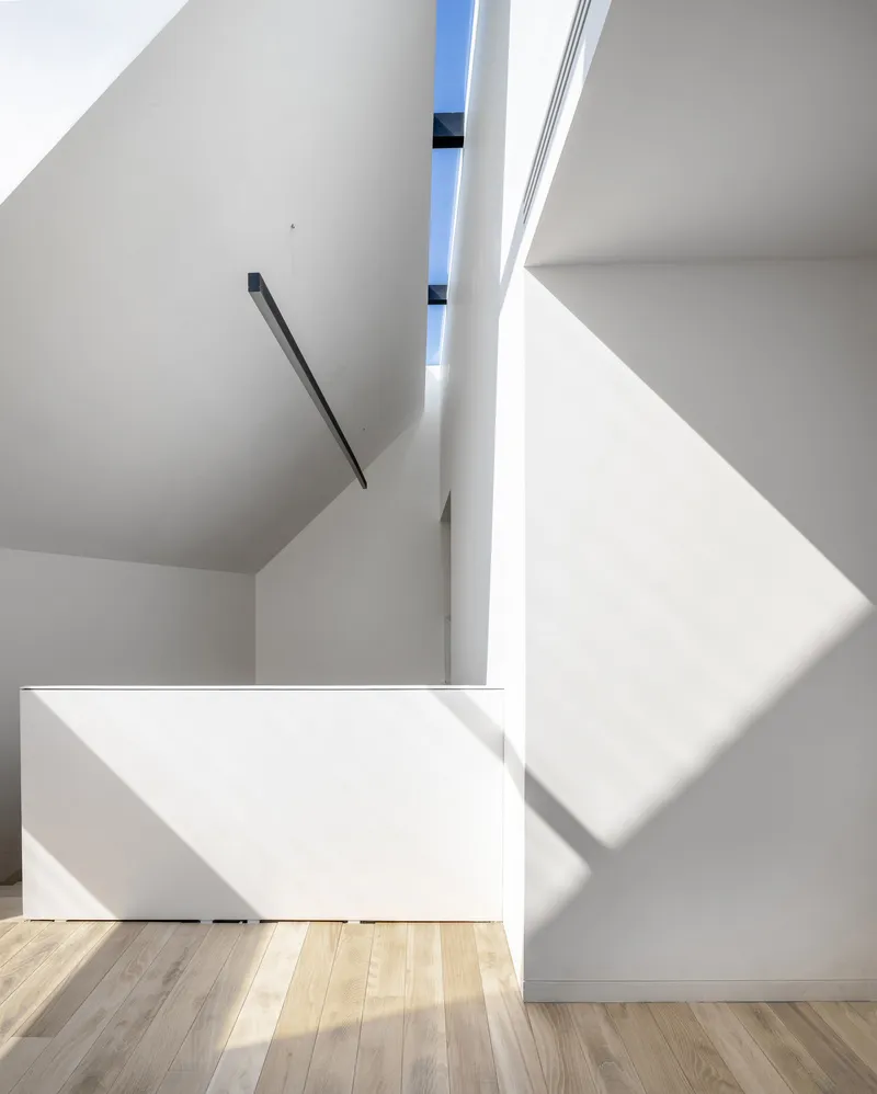 Angled stairwell with black metal handrail and sunlight casting sharp shadows across white surfaces