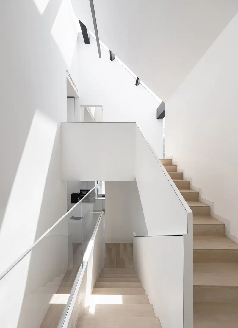 Multi-level staircase with light wood treads and white walls flooded with natural light