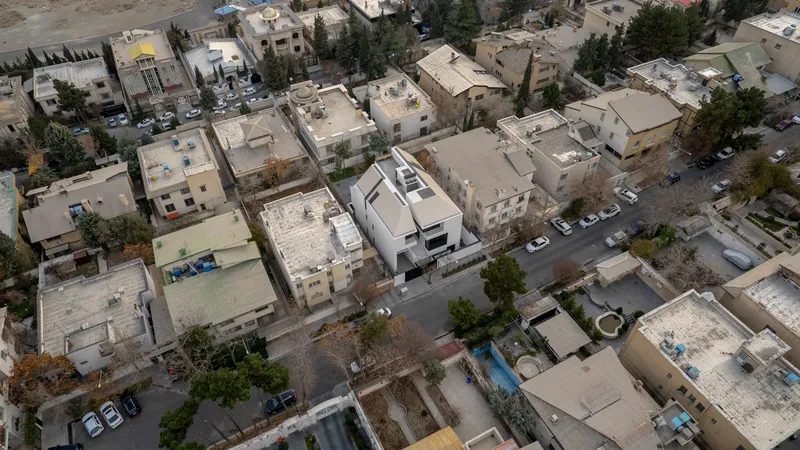 Aerial view of white rooftop volumes surrounded by residential blocks and parked cars