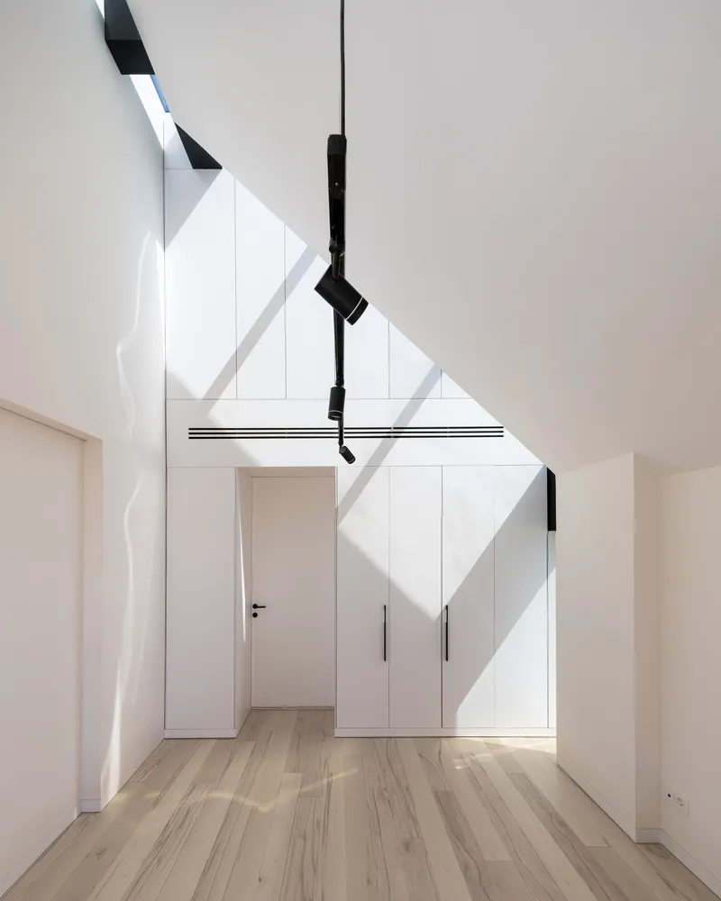 White storage wall beneath a staircase with diagonal shadows cast by overhead skylights