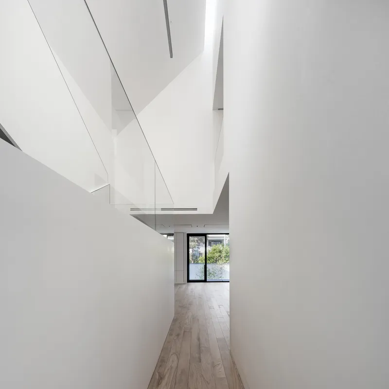 Corridor with angled white walls and skylights leading toward a glazed door with garden beyond
