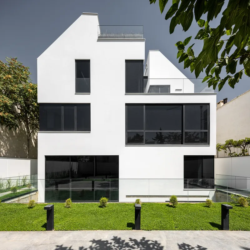 White rendered facade with dark glazing and lawn garden framed by overhanging tree branches