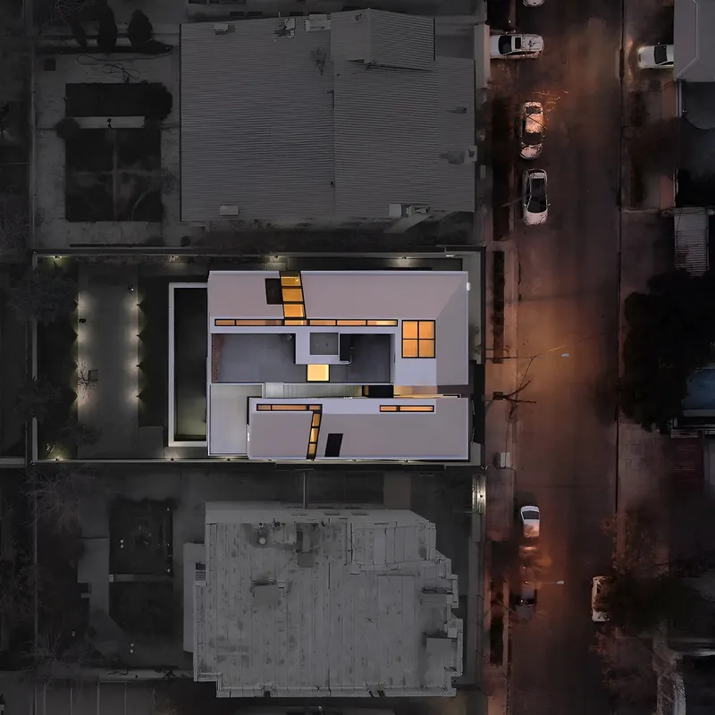 Aerial view at dusk showing illuminated roof planes and parked cars along the street