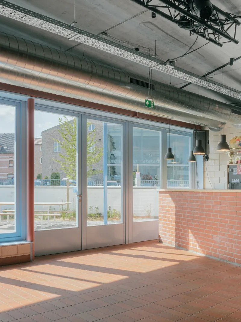 Interior with terracotta floor tile and brick service counter below exposed mechanical ducts and pendant lights