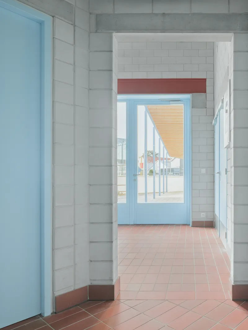 Interior corridor with white tile walls, terracotta flooring and pale blue door framing an exterior porch