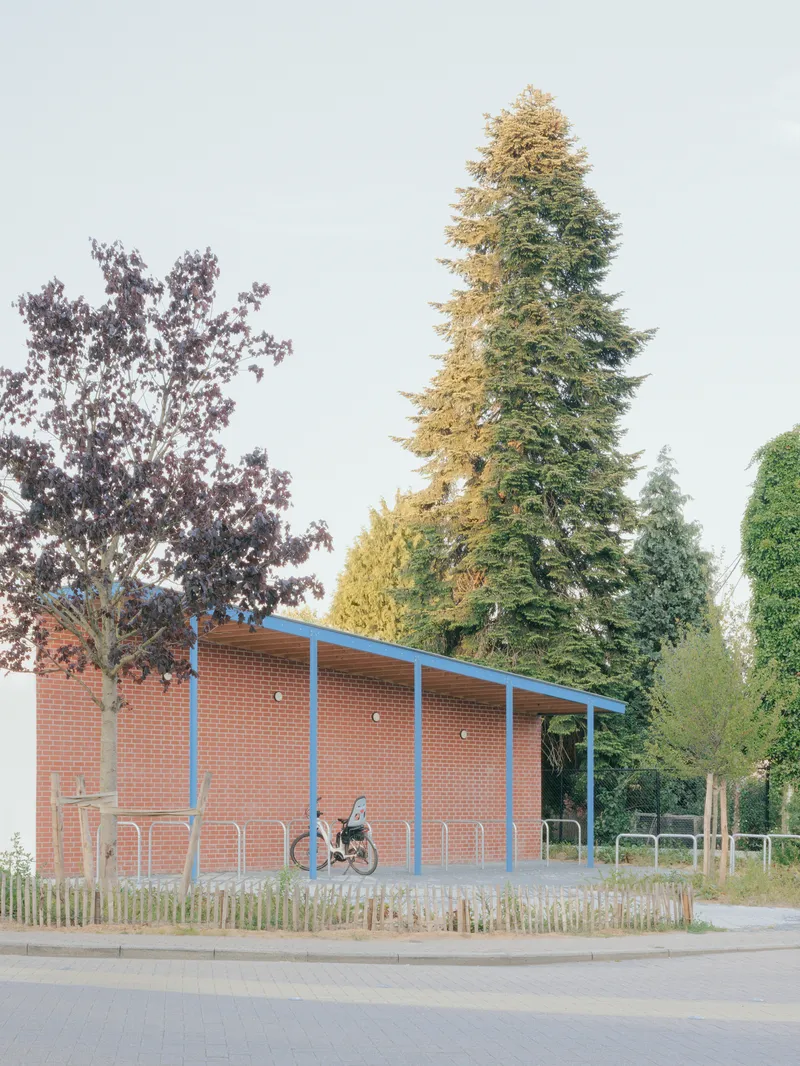 Brick bike shelter with sloped roof and cyclist passing under autumn foliage