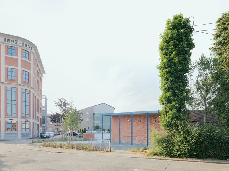 Street view of brick pavilion with blue trim beside curved facade and trees