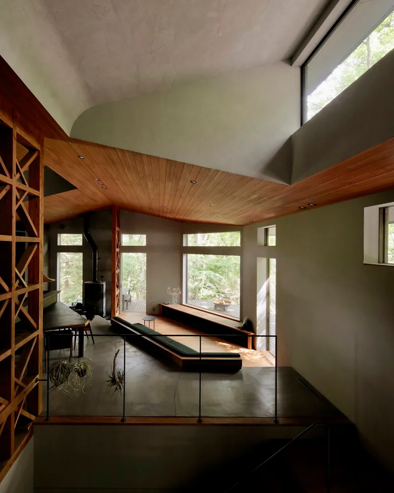 Double-height living space with wood slat ceiling and glass railings overlooking the forest