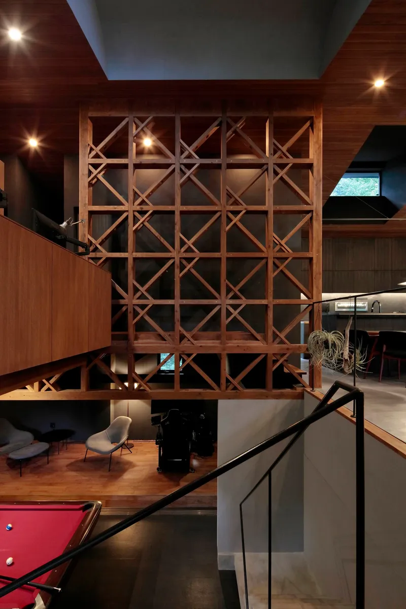 Double-height interior showing a freestanding timber lattice screen between wood-clad mezzanines under recessed lighting