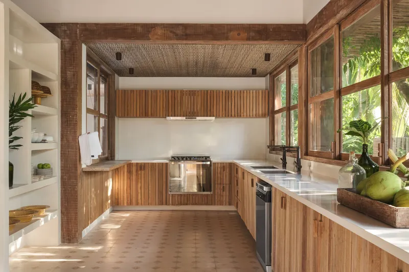 Kitchen with vertical timber cabinetry, woven ceiling panel and windows framing banana palms outside