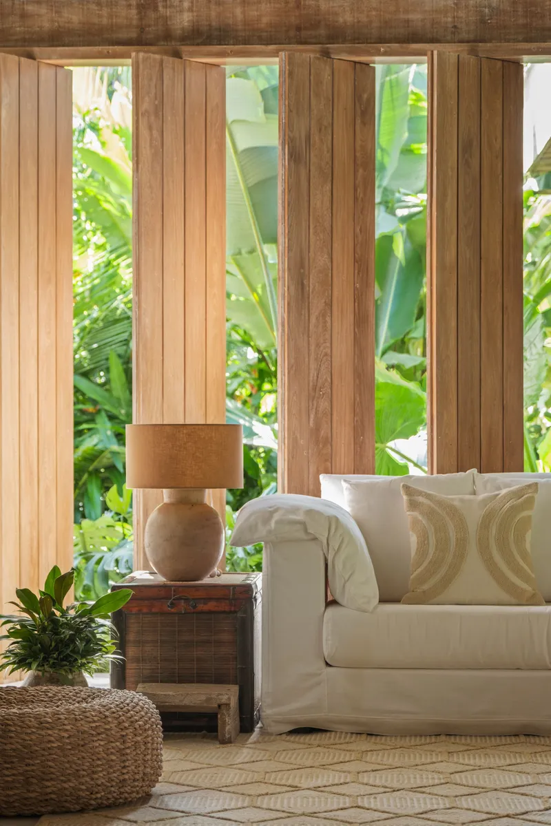 Vertical timber slat wall with glazed openings framing tropical foliage in afternoon light