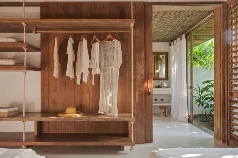 Bedroom closet with rope-suspended bench, hanging garments and view through to ensuite bathroom