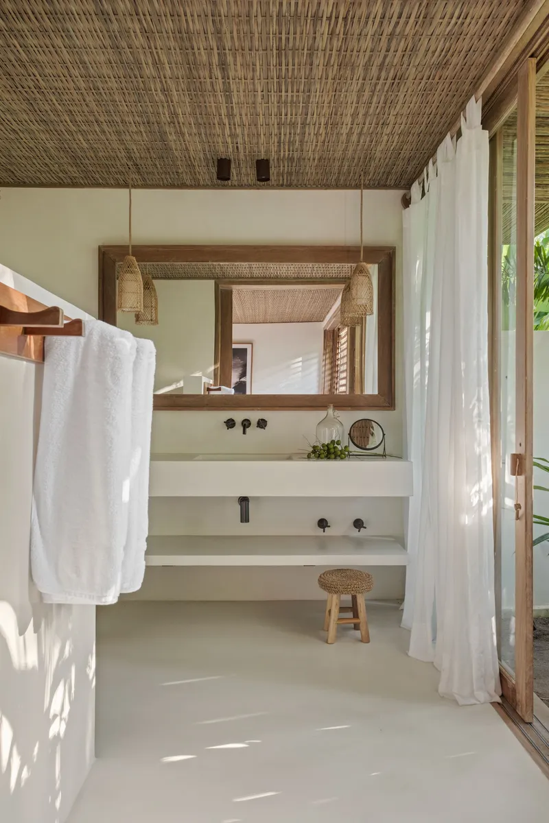 Bathroom vanity with woven ceiling and white curtains filtering dappled sunlight onto polished concrete floor