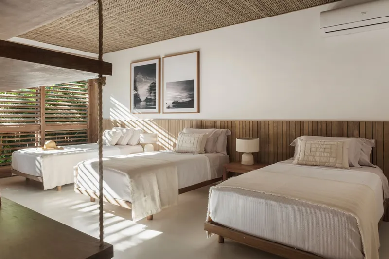 Twin bedroom with timber louvered shutters casting striped shadows across the polished floor