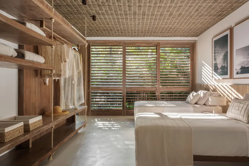 Bedroom interior with woven bamboo ceiling and louvered timber doors overlooking tropical vegetation
