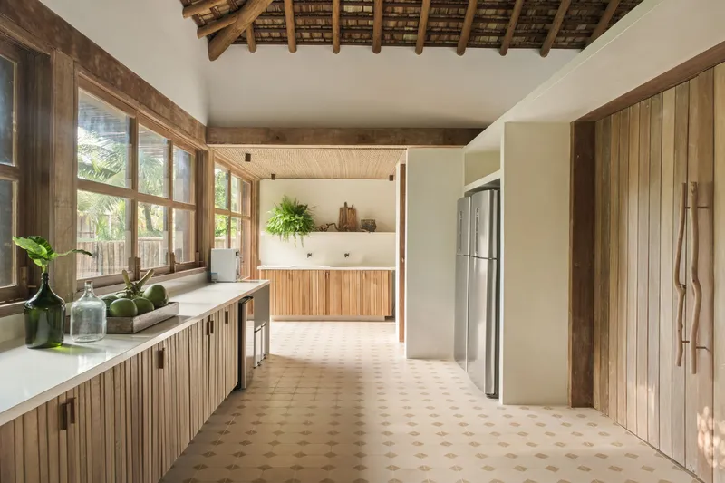 Kitchen passage with patterned terracotta floor tiles and vertical timber-clad cabinetry under exposed rafters