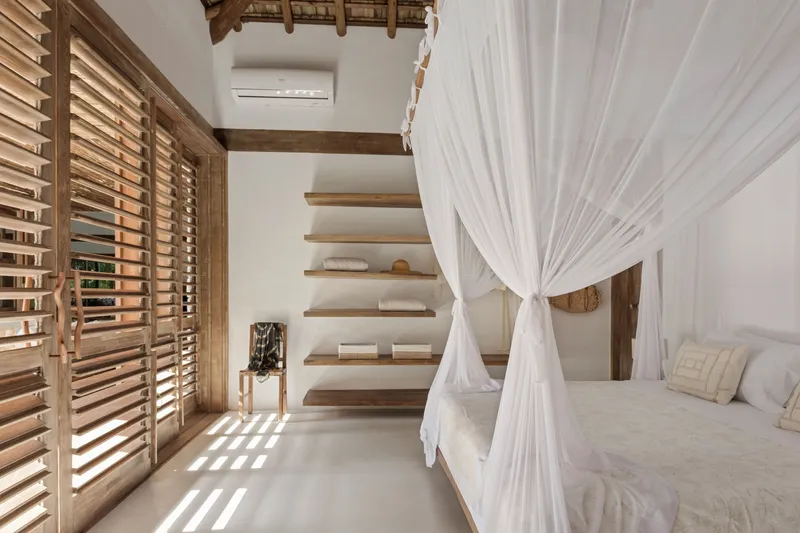 Floating timber staircase beside louvered shutters with mosquito netting draped around a bed frame