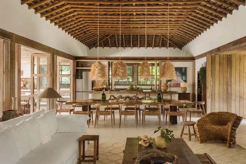 Open plan dining and living area beneath exposed timber rafters with woven pendant lights overhead