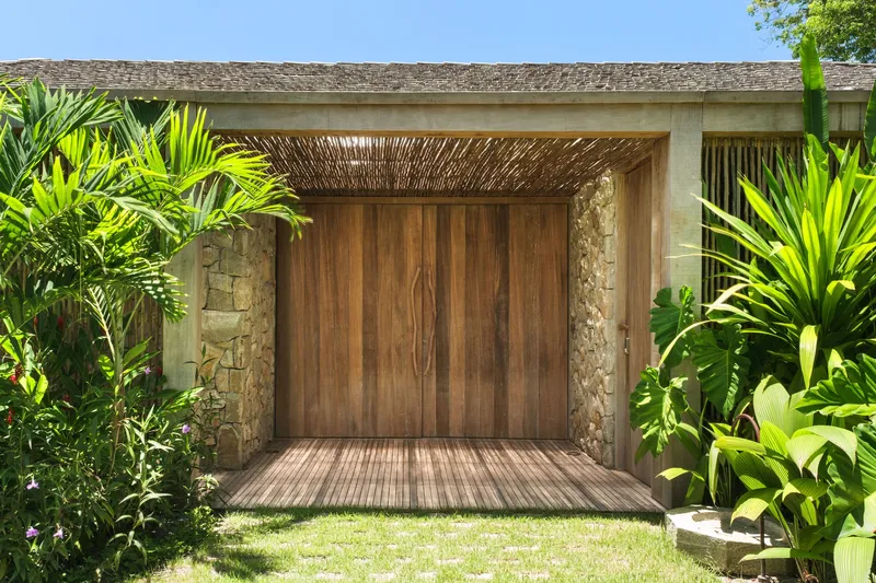 Covered entrance with timber doors, stone walls and woven wood ceiling surrounded by tropical plantings