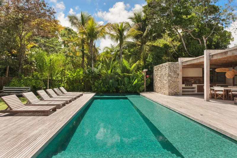 Pool deck with timber loungers beside green tiled water under palm trees and blue sky