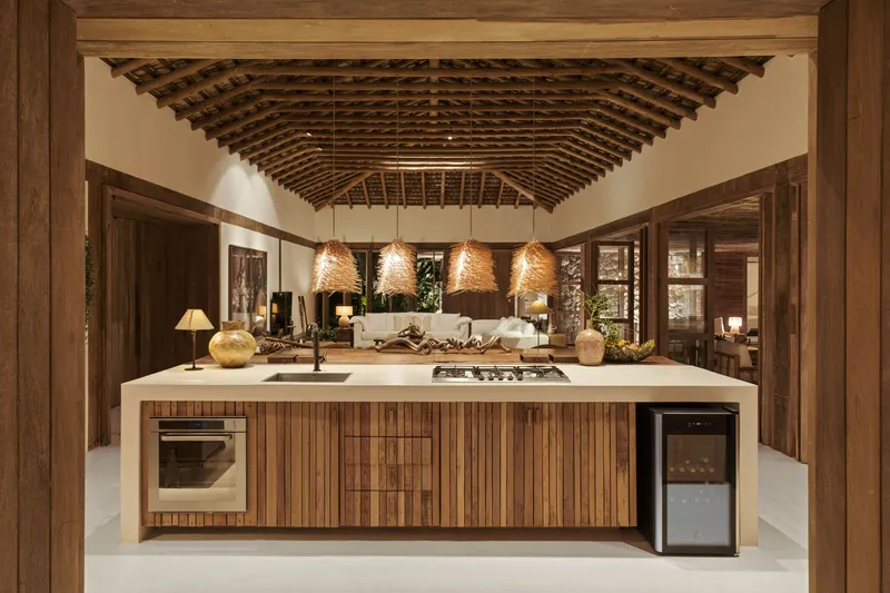 Kitchen island with timber cabinetry beneath exposed timber roof trusses and woven pendant lamps