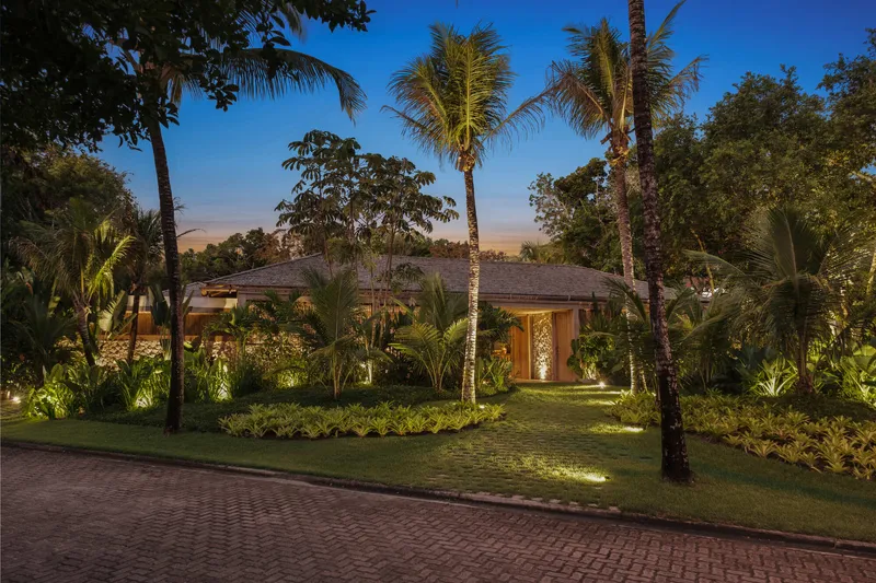Low-pitched roof volume amid landscaped lawn and palm trees lit at twilight