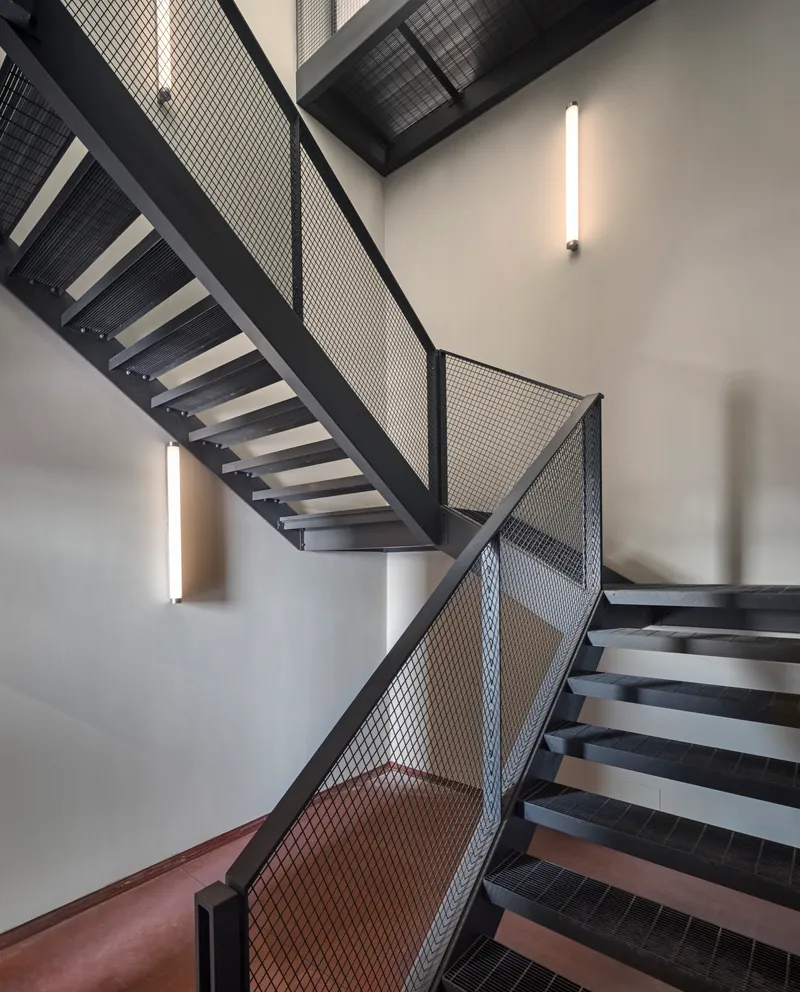 Black steel staircase with mesh balustrades and wall-mounted linear light fixtures