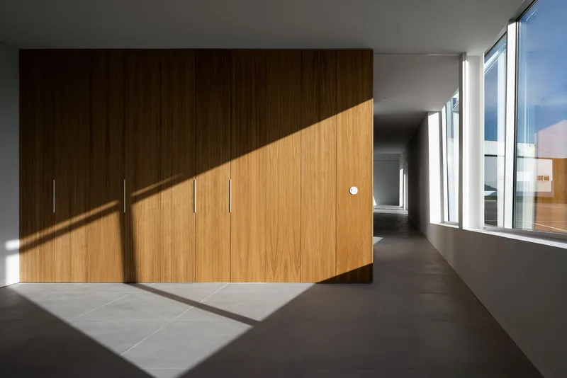 Warm timber volumes contrasted by sharp natural light entering the corridor.