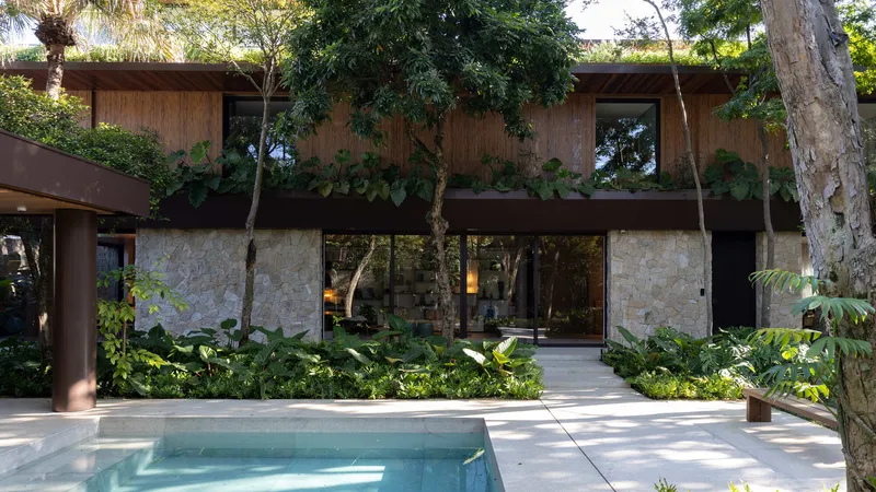 Two-storey facade with stone base and timber upper volume facing a pool deck surrounded by tropical planting