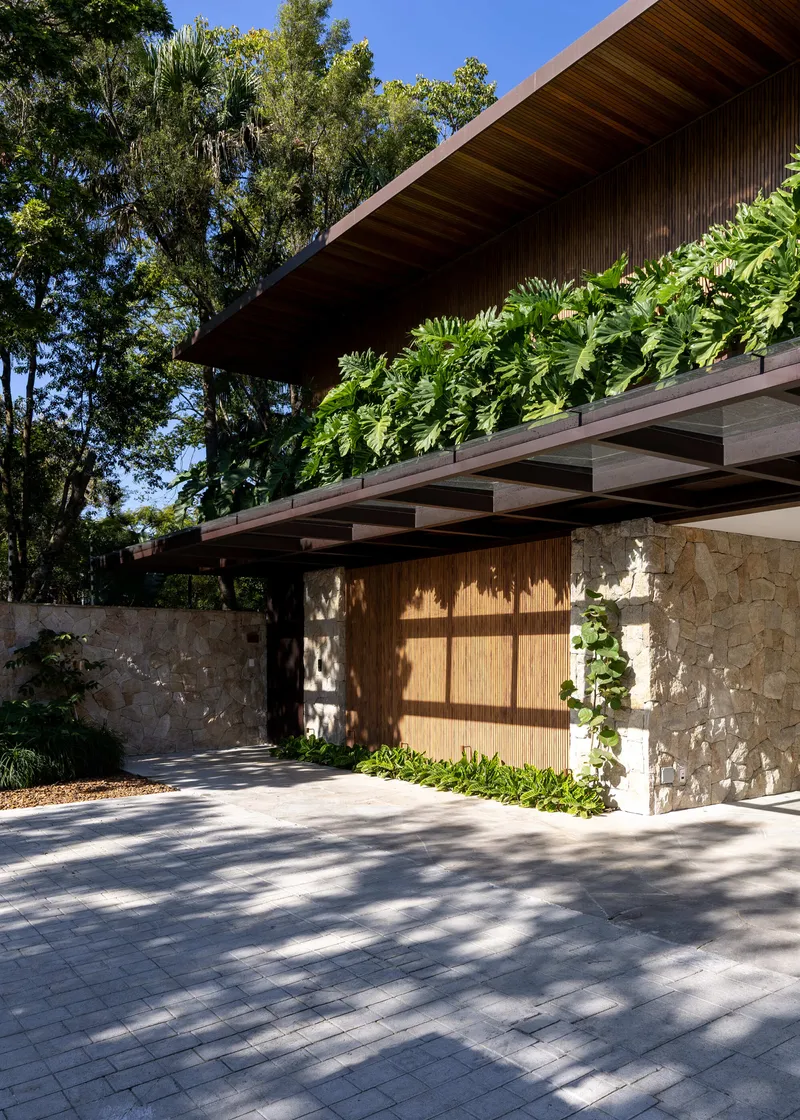 Entrance with timber slat screen flanked by stone walls beneath a deep overhang with exposed beams and ferns