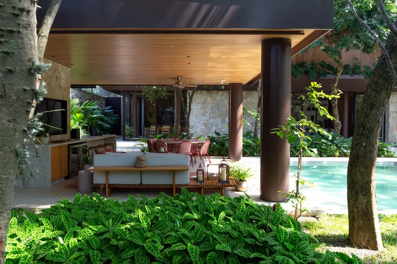 Open living pavilion with timber ceiling and cylindrical column opening to pool and garden through existing trees