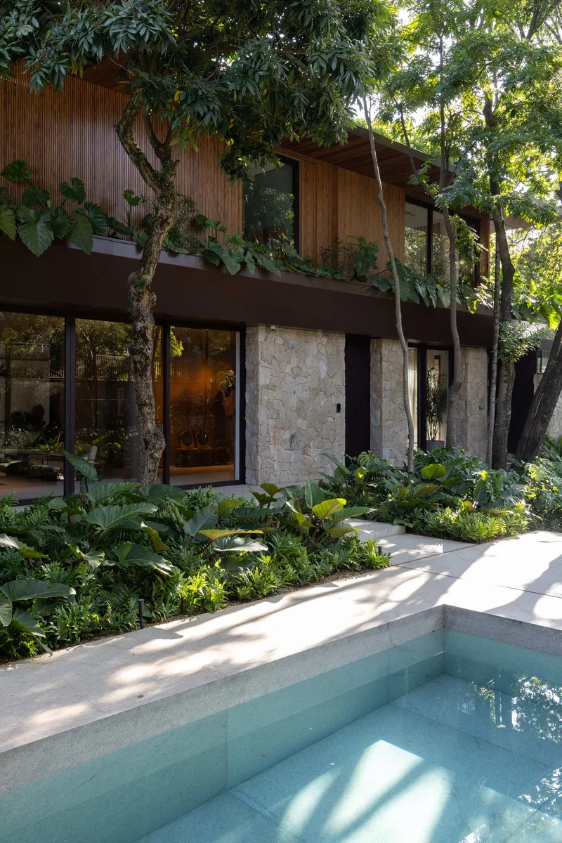 Corner of pool with stone coping adjacent to planted beds and two-storey facade behind trees