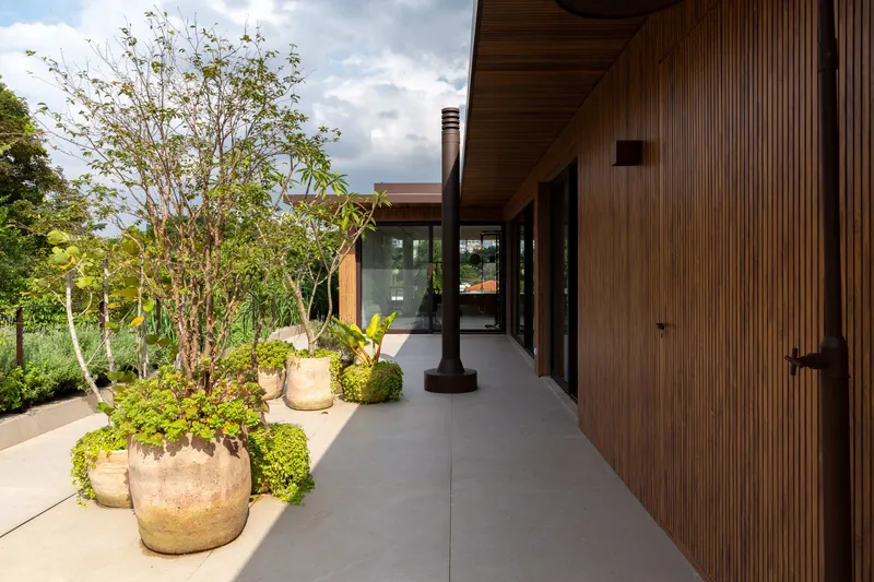 Covered terrace with vertical timber cladding, large planters with trees, and a black cylindrical column