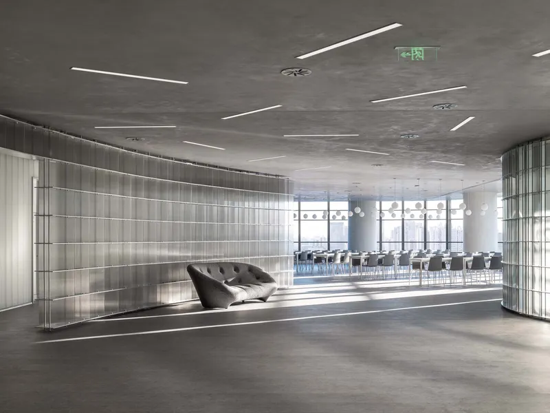 Reception lounge with translucent vertical panel walls and a dark tufted sofa beneath linear ceiling lights