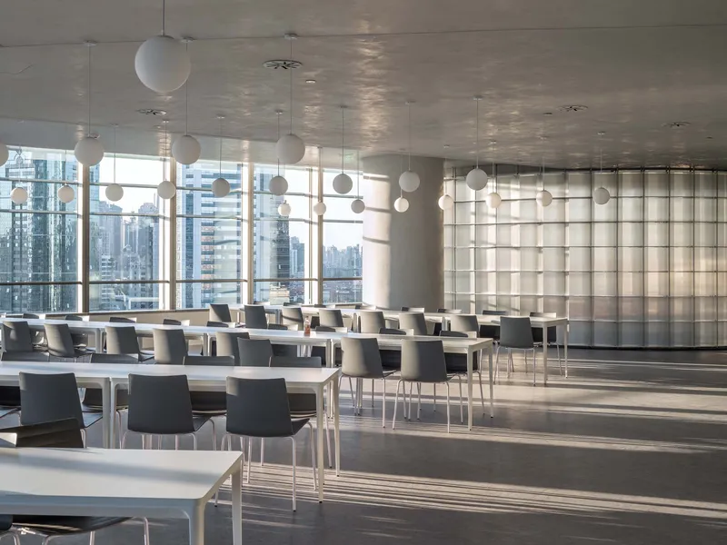Cafeteria with rows of white tables and chairs beneath sphere pendant lights and bright city views