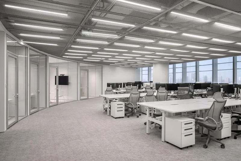 Open-plan workspace with white desks and exposed metal mesh ceiling panels with linear lighting