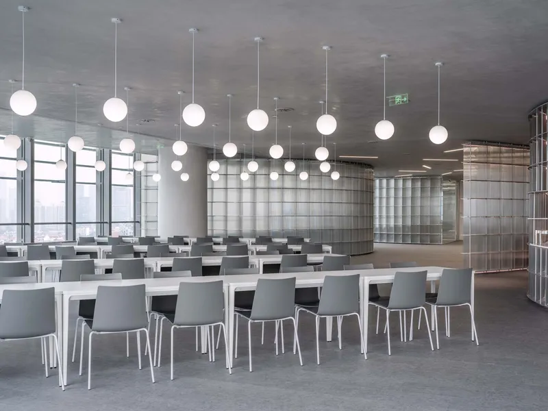 Dining hall with white tables, gray chairs, and rows of spherical pendant lights under cloudy sky
