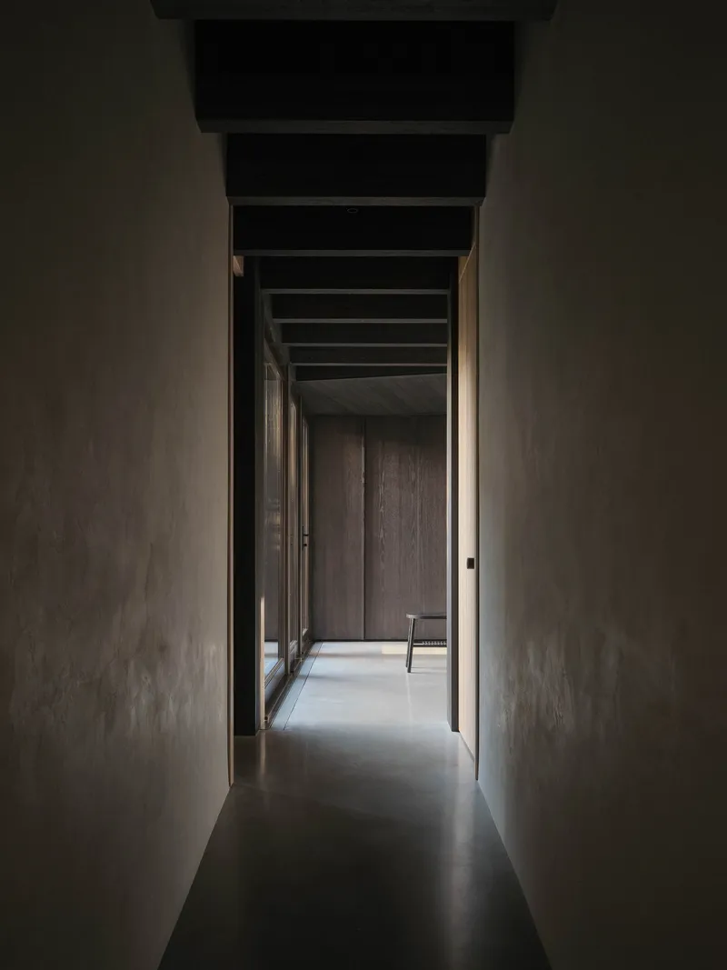 Narrow corridor with polished concrete floor and exposed ceiling beams framed by smooth plaster walls