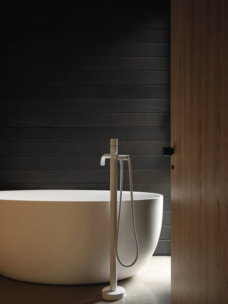 Freestanding tub with floor-mounted faucet against horizontal black timber cladding