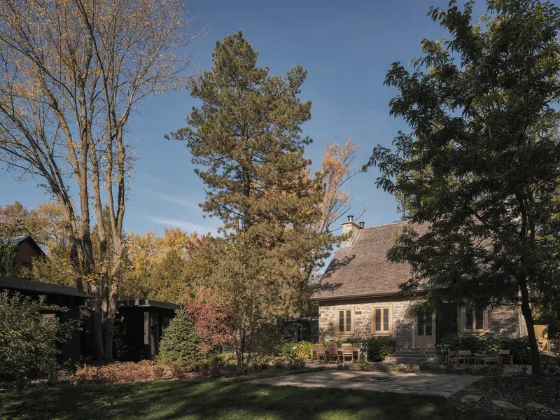 Courtyard view showing stone masonry volume with timber extension wing under autumn foliage