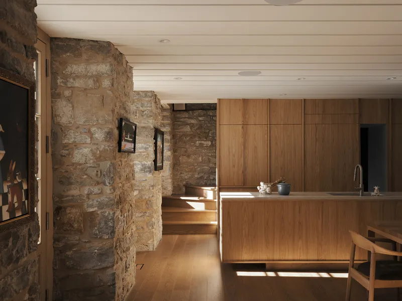 Kitchen with timber cabinetry and island against exposed stone walls under a white plank ceiling