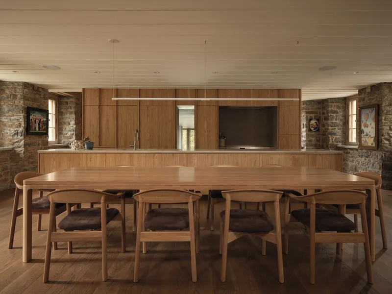 Open kitchen and dining area with timber cabinetry, pendant light, and stone walls framing narrow windows