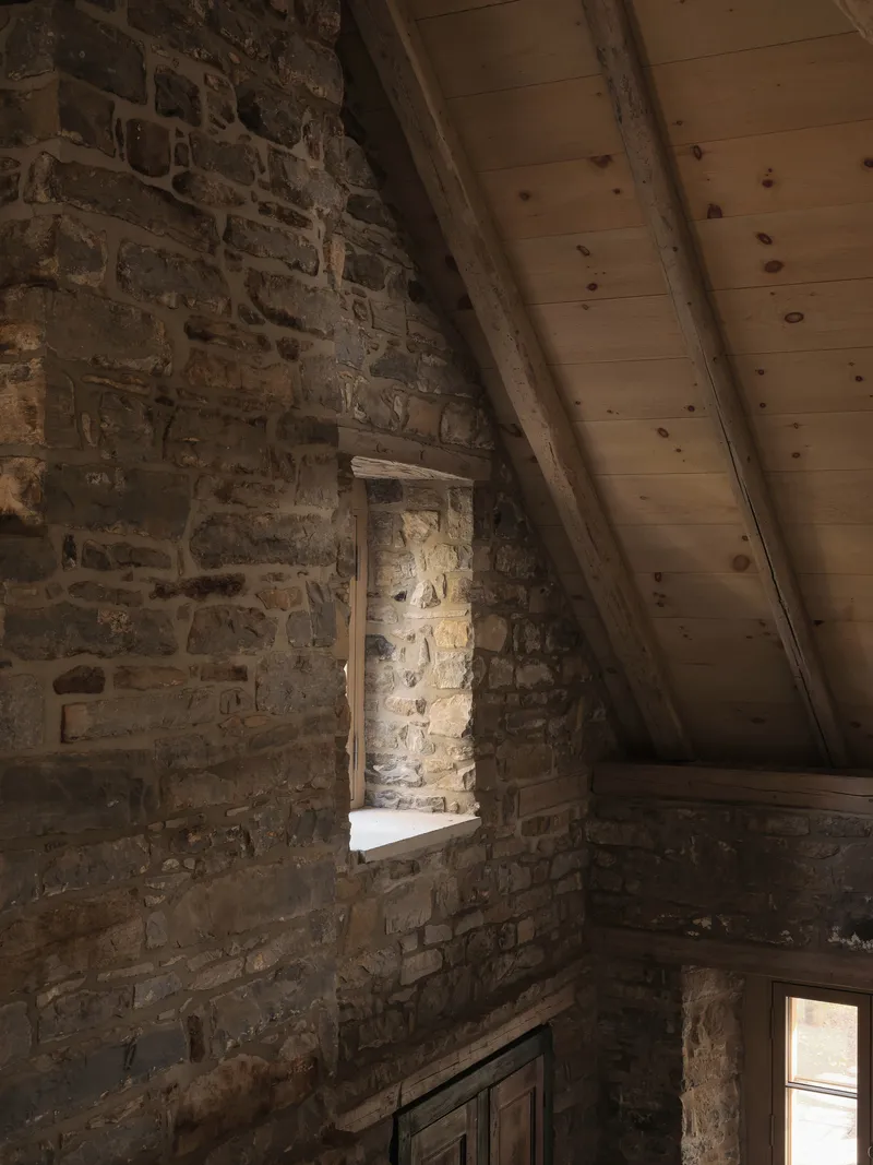 Stone masonry wall with recessed niche beneath exposed timber ceiling beams and planking